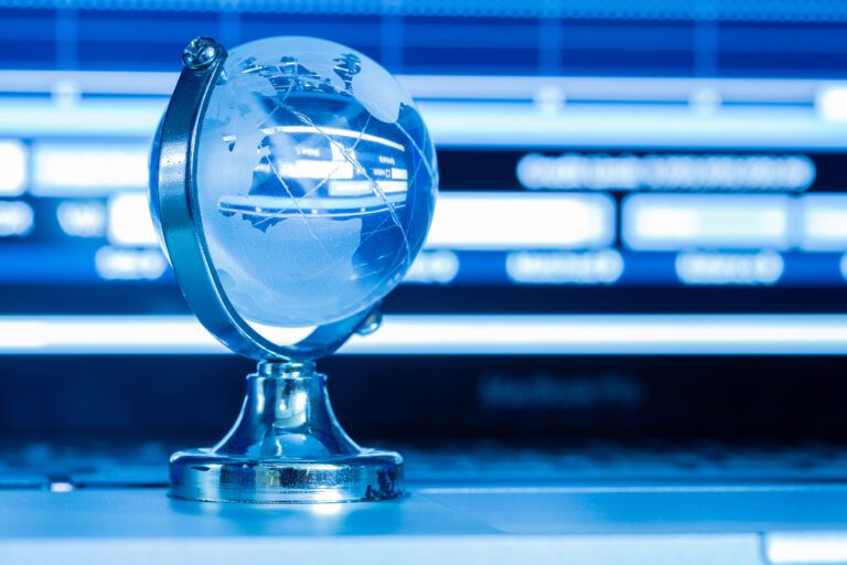 A small, transparent globe with a silver stand sits on a laptop keyboard. The background features a blue, defocused computer screen displaying various charts and graphs, subtly suggesting themes of global technology or digital data, possibly connected to kemoIPTV channel lists.