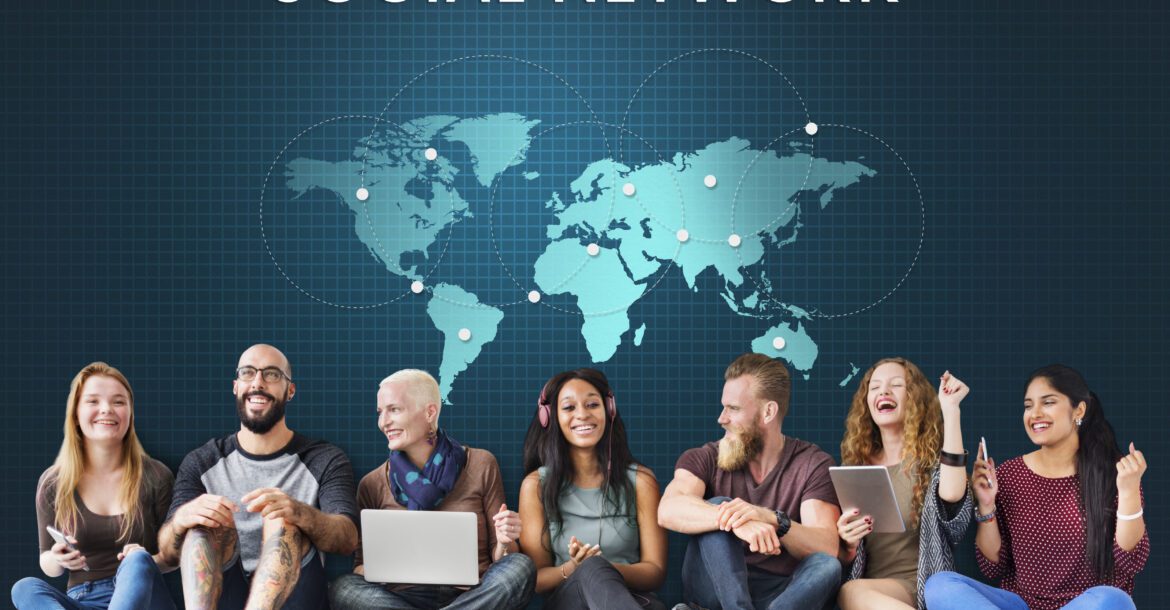A diverse group of seven people are sitting in a row, smiling, and using various electronic devices. Against a blue world map background displaying interconnected locations with the text "SOCIAL NETWORK" above them, some of them seem to be watching KemoTV together.
