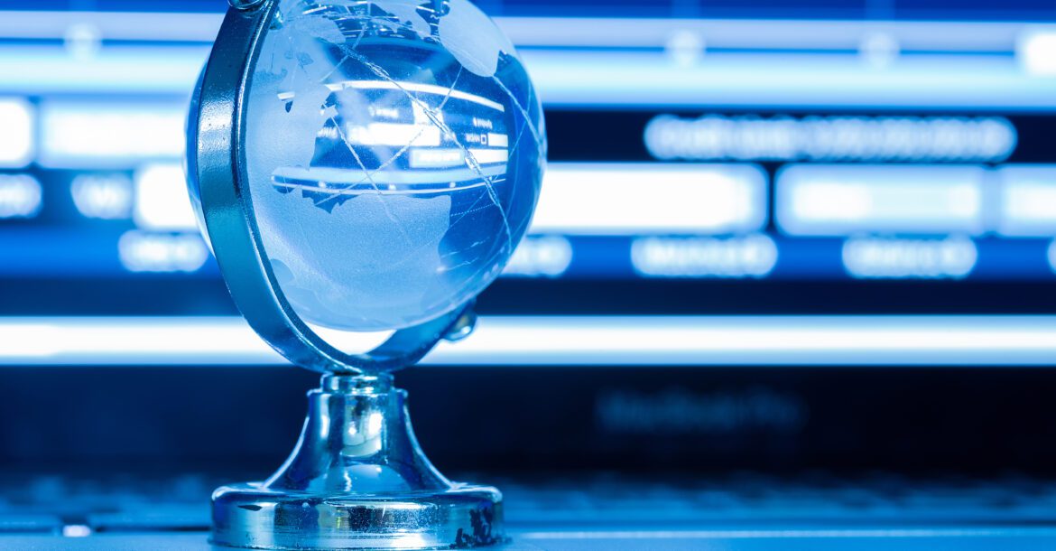 A small, transparent globe with a silver stand sits on a laptop keyboard. The background features a blue, defocused computer screen displaying various charts and graphs, subtly suggesting themes of global technology or digital data, possibly connected to kemoIPTV channel lists.